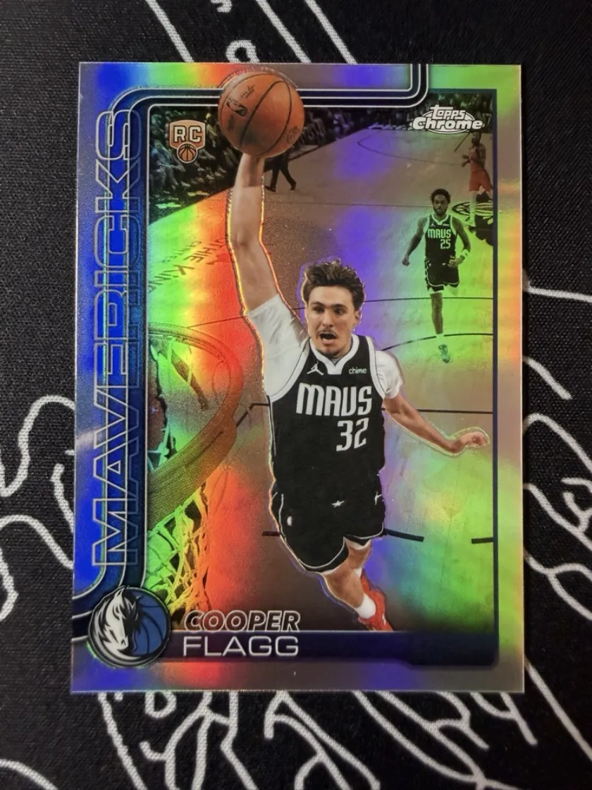 The front of the card: Cooper Flagg in a Mavericks jersey, on a rainbow refractor finish, photographed flat on a dark cloth.